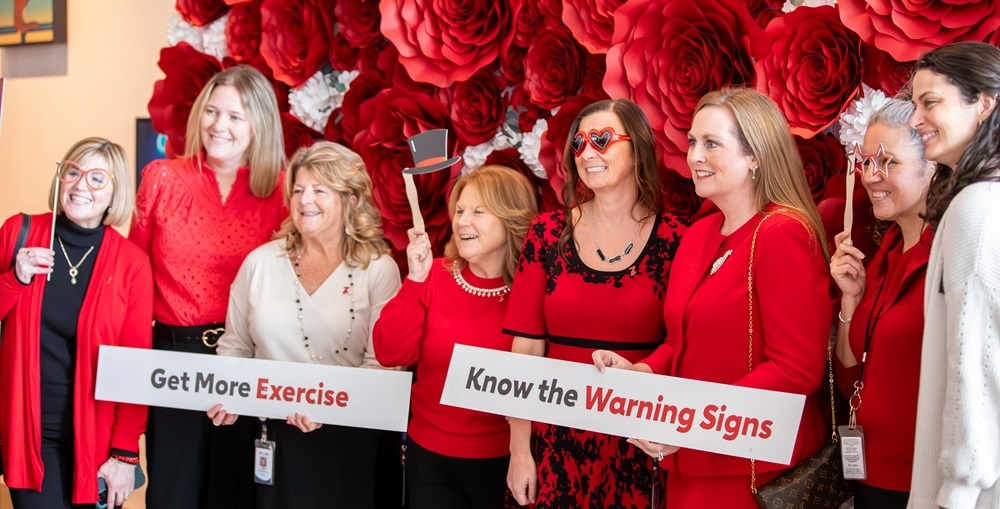 Group of women in red holding up signs reading 'Get more exercise' and 'Know the warning signs'.